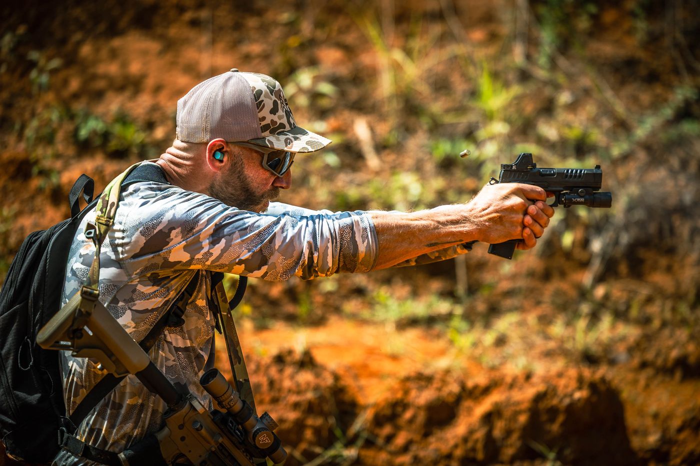 A competitor firing a pistol with a carbine slung