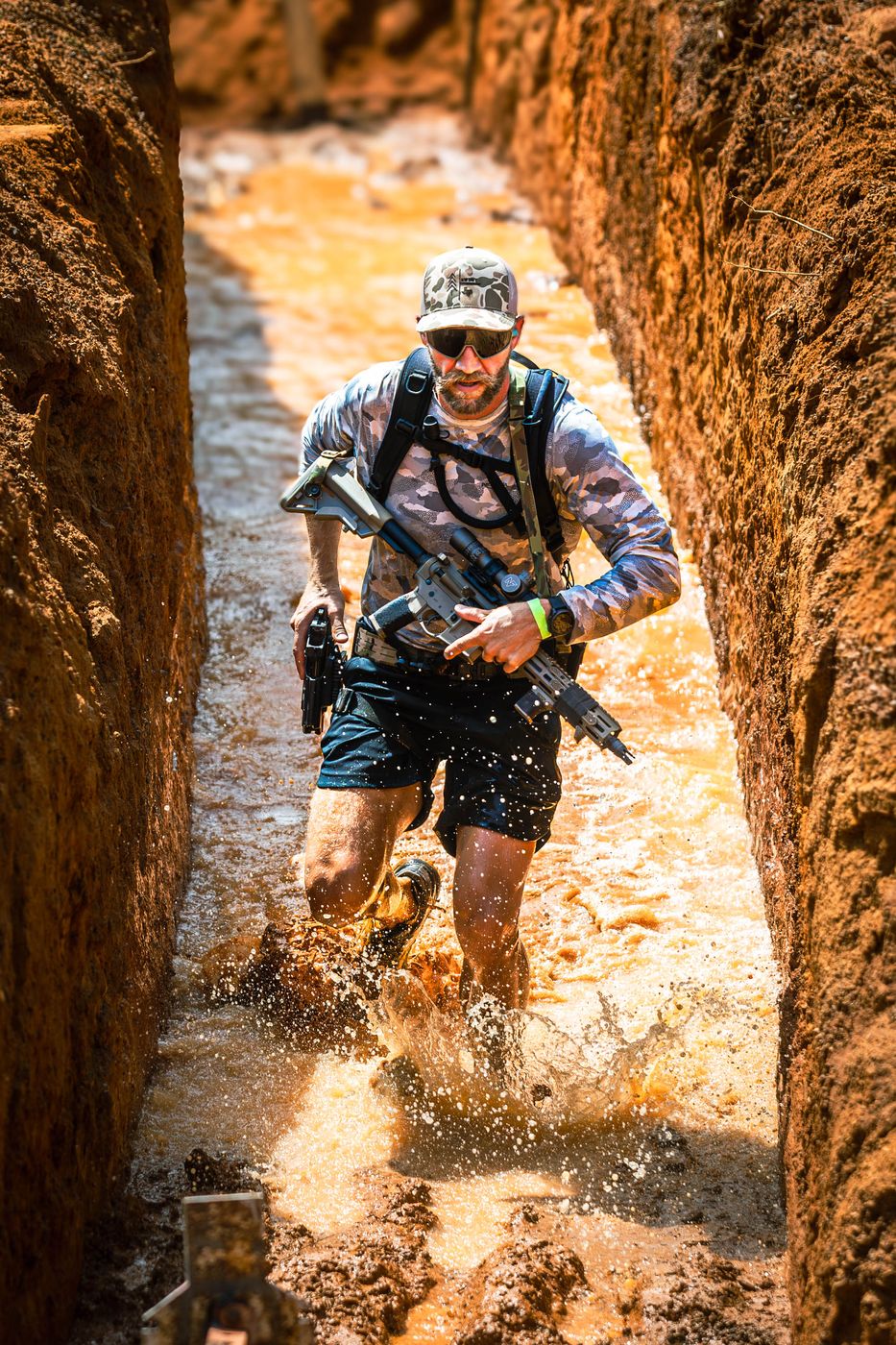 A competitor running through a flooded trench with a carbine